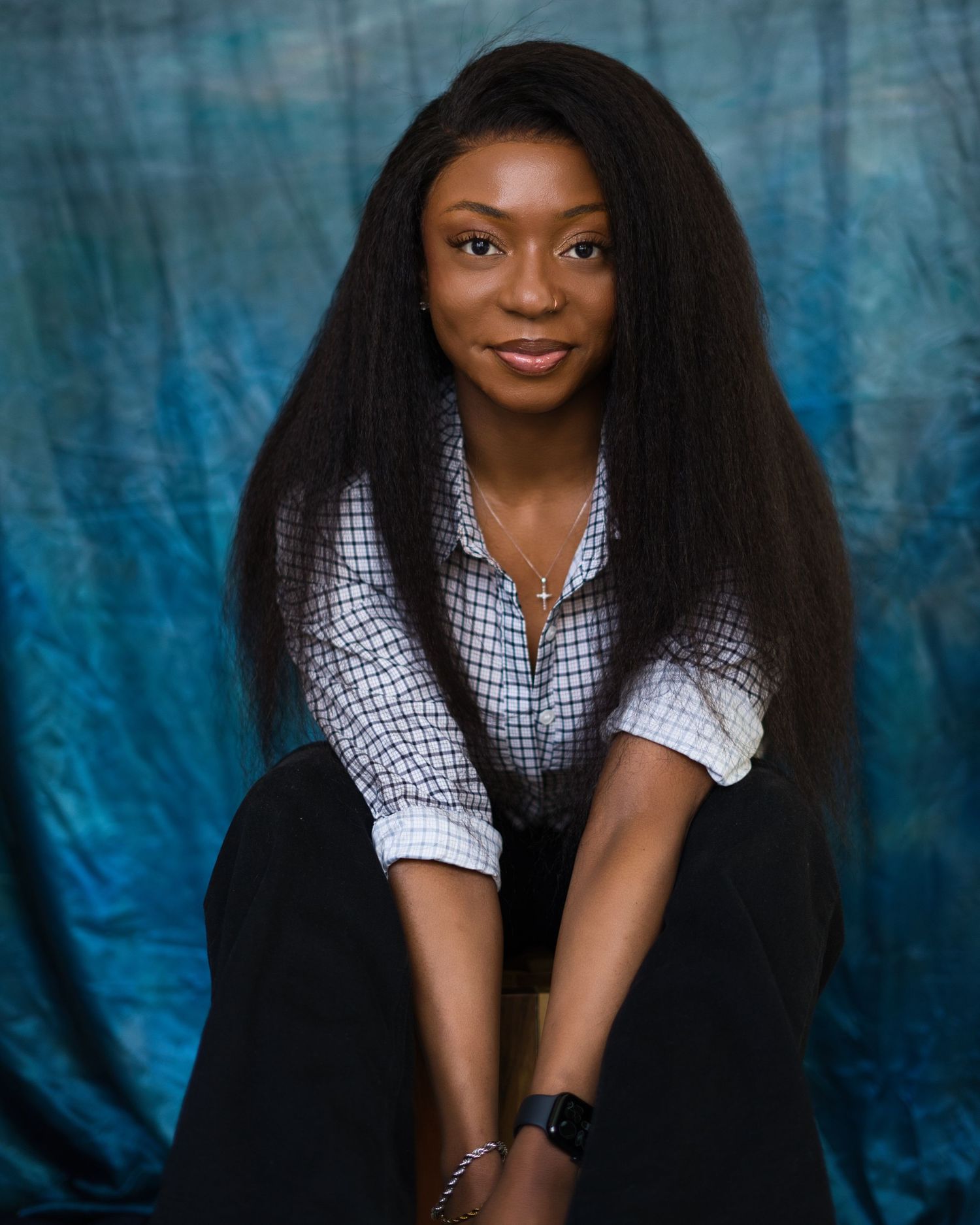 Professional studio portrait against a blue backdrop featuring someone in a checkered button-down shirt and long dark hair.