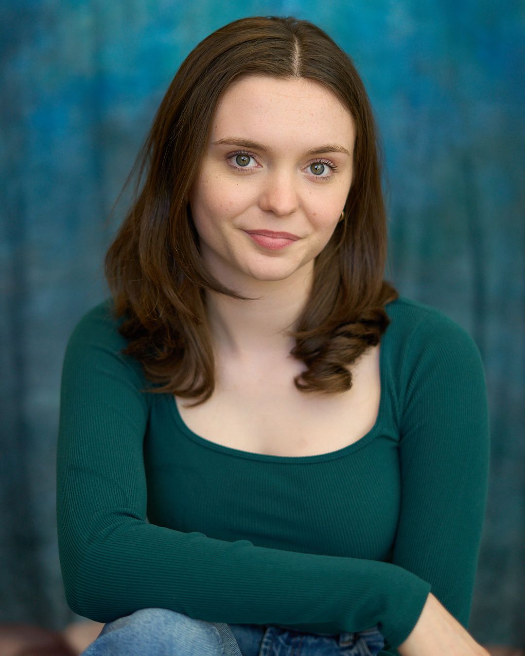 Young woman with brown hair wearing a green long-sleeve top, posing for a professional headshot photo.