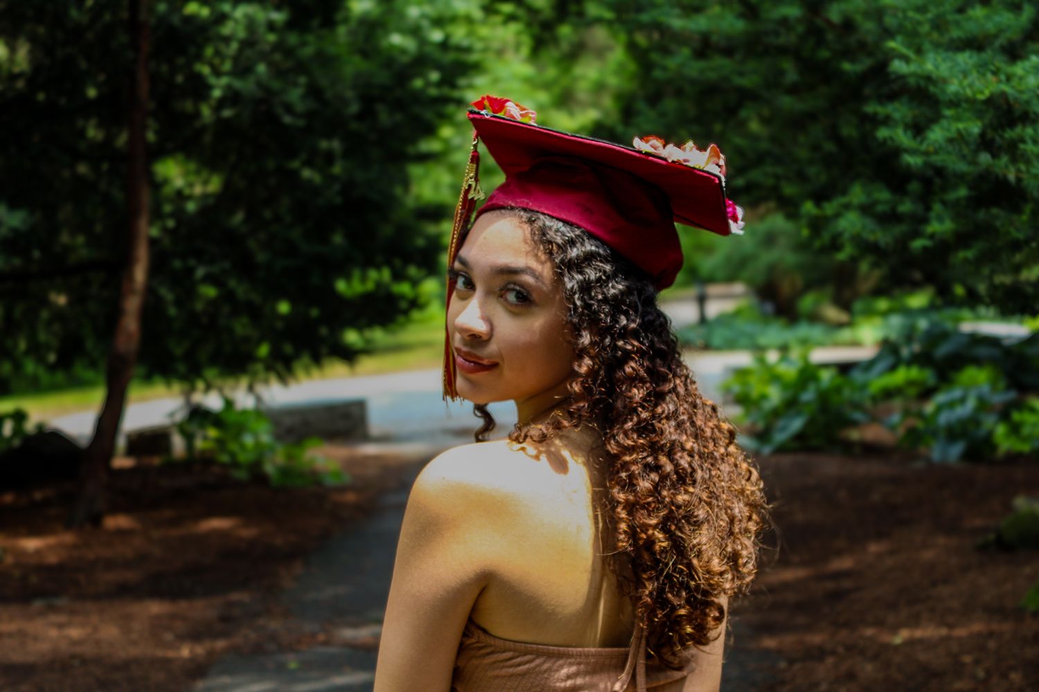 Graduate in red cap poses in natural wooded setting.