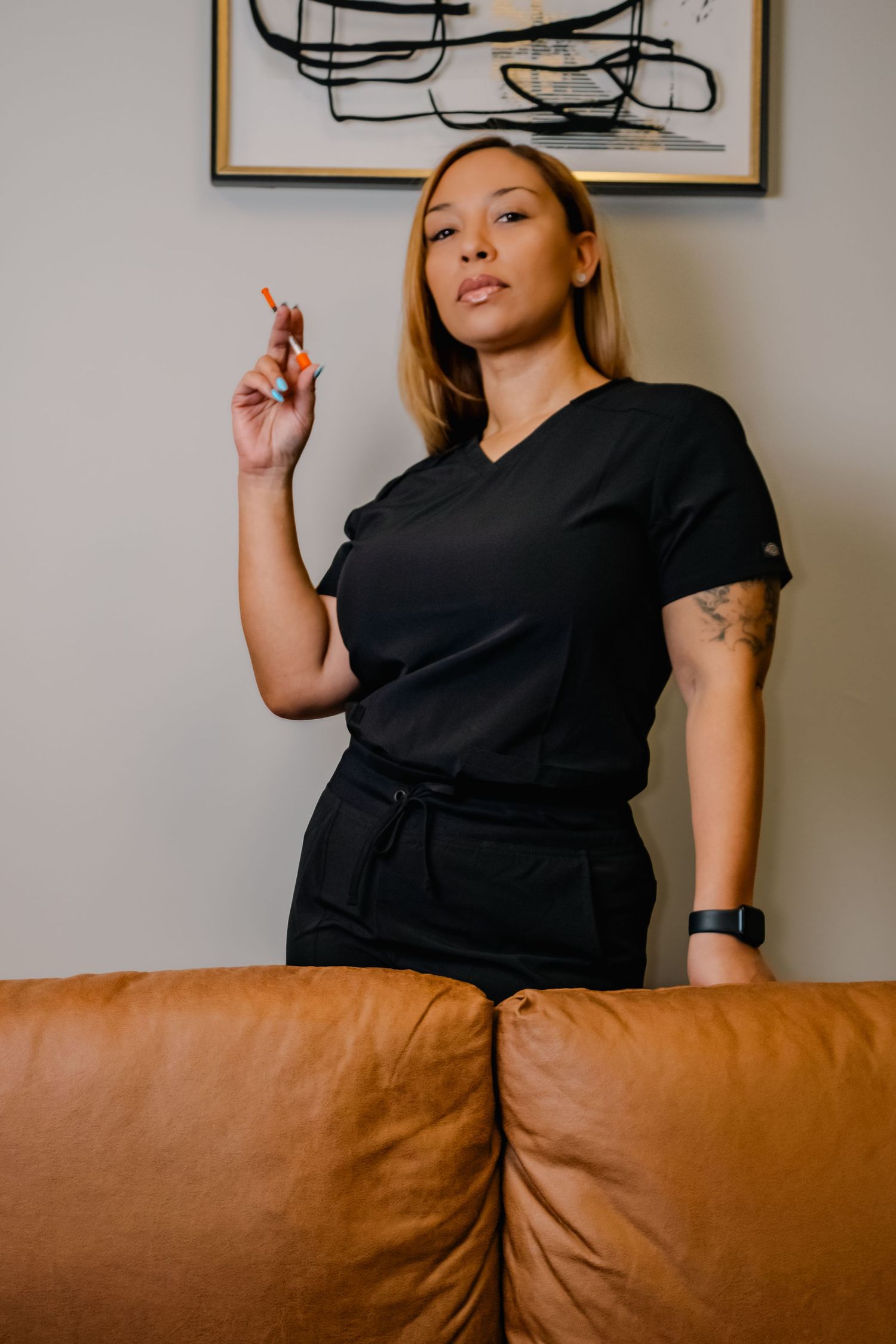 Woman in black attire standing by brown couch with abstract art in background.