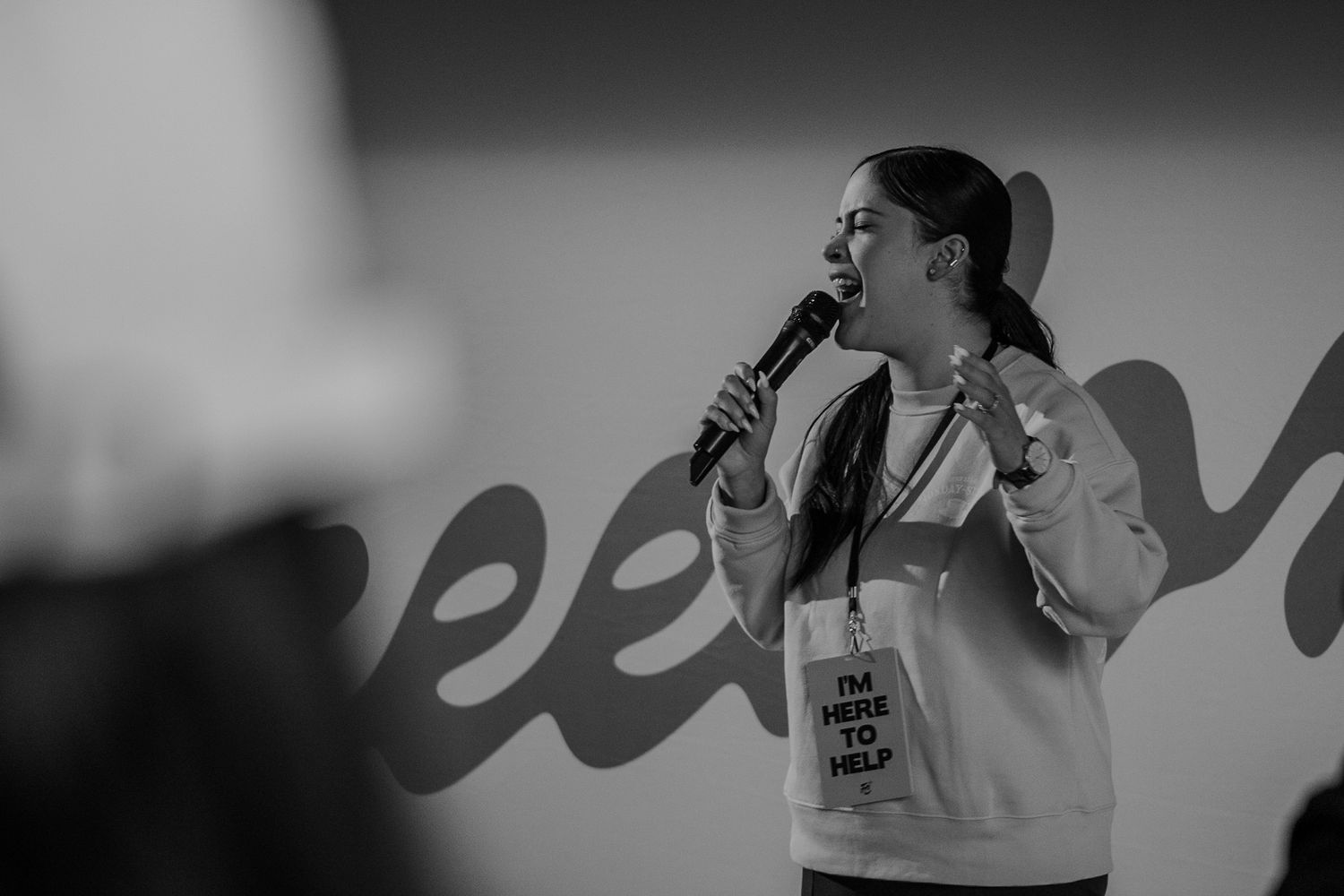 Speaker in hoodie and cap performs energetically in black and white photo.