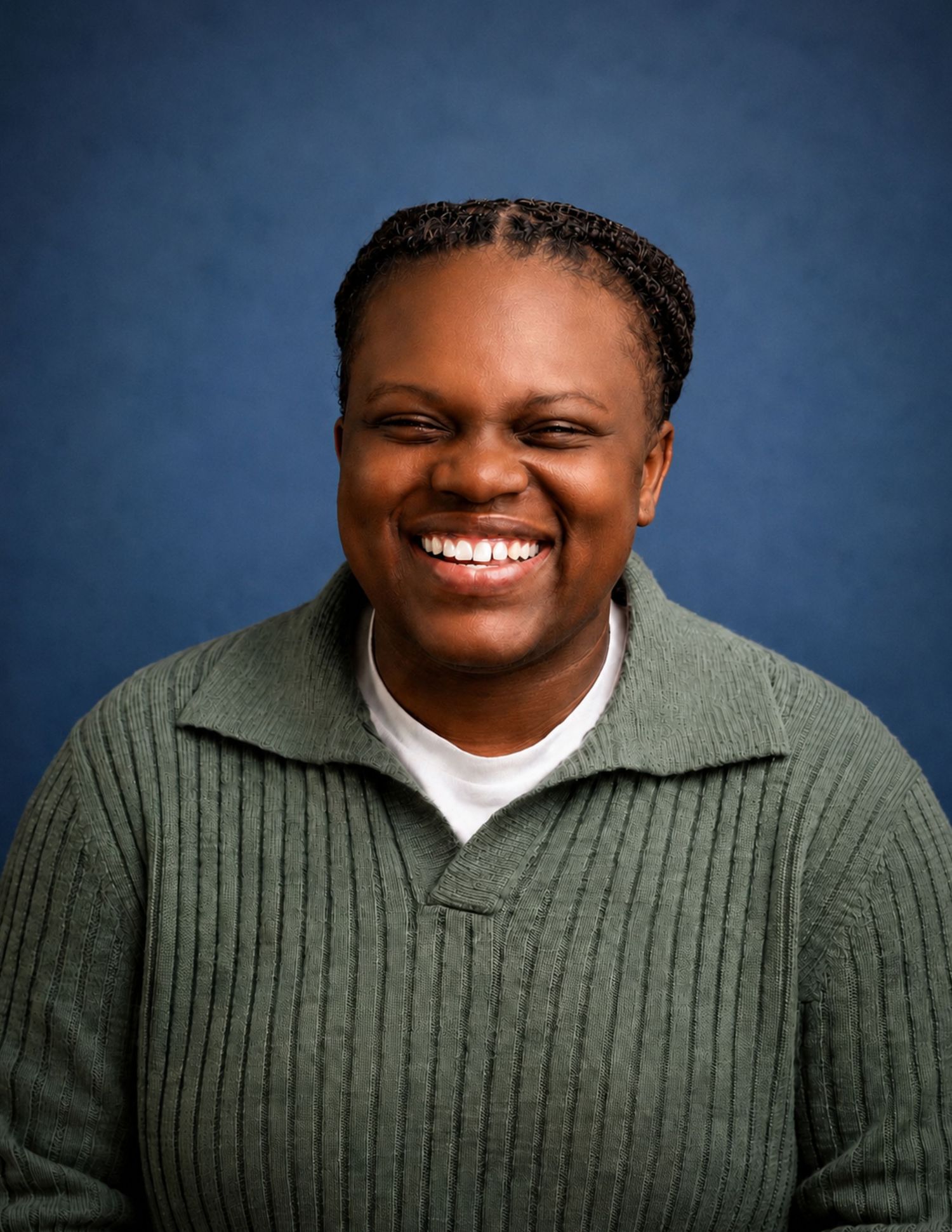 Smiling person with braids wearing a green sweater poses for a professional headshot against a blue background.