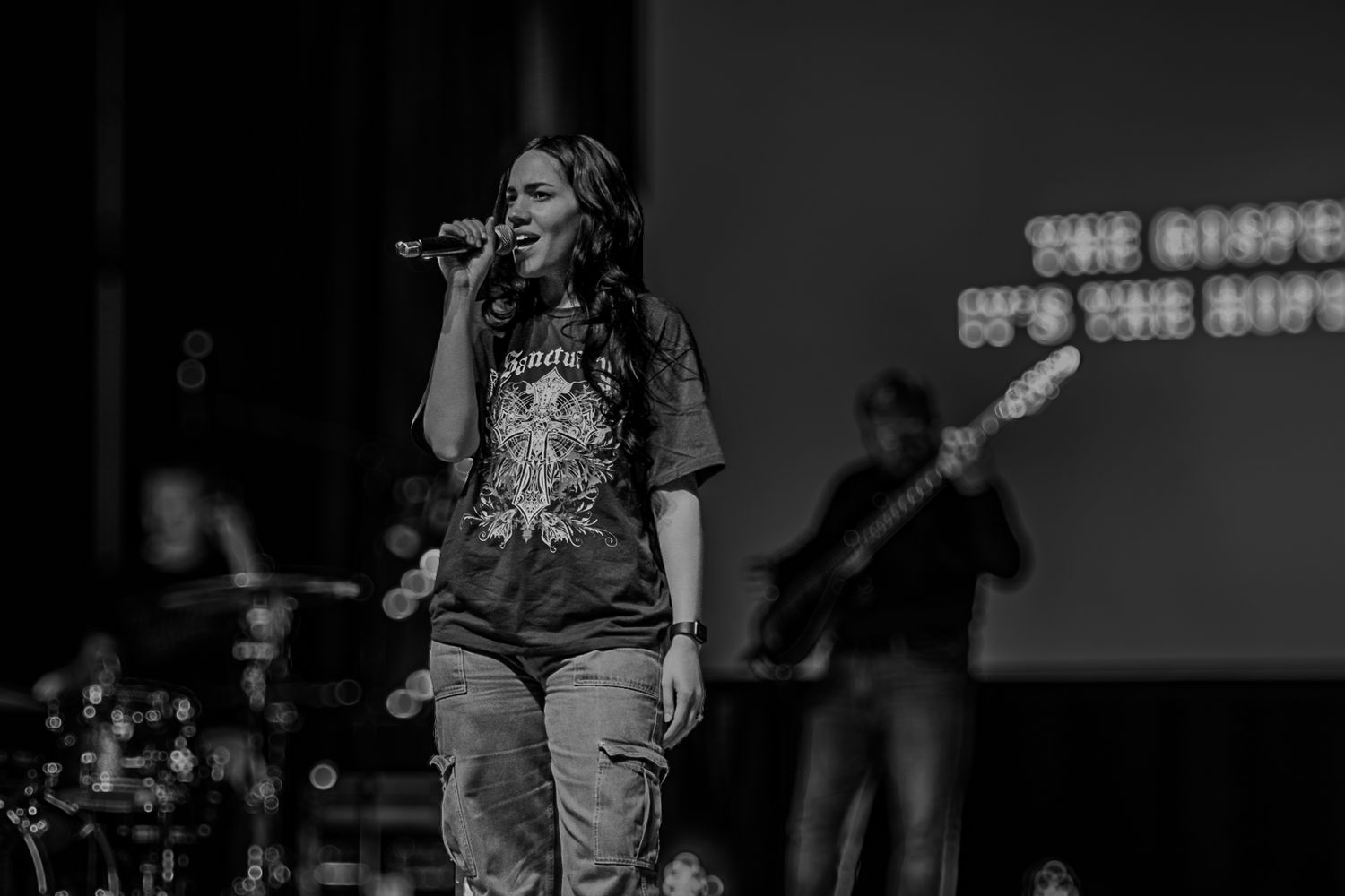 Black and white photo of a performer singing on stage with band in background.