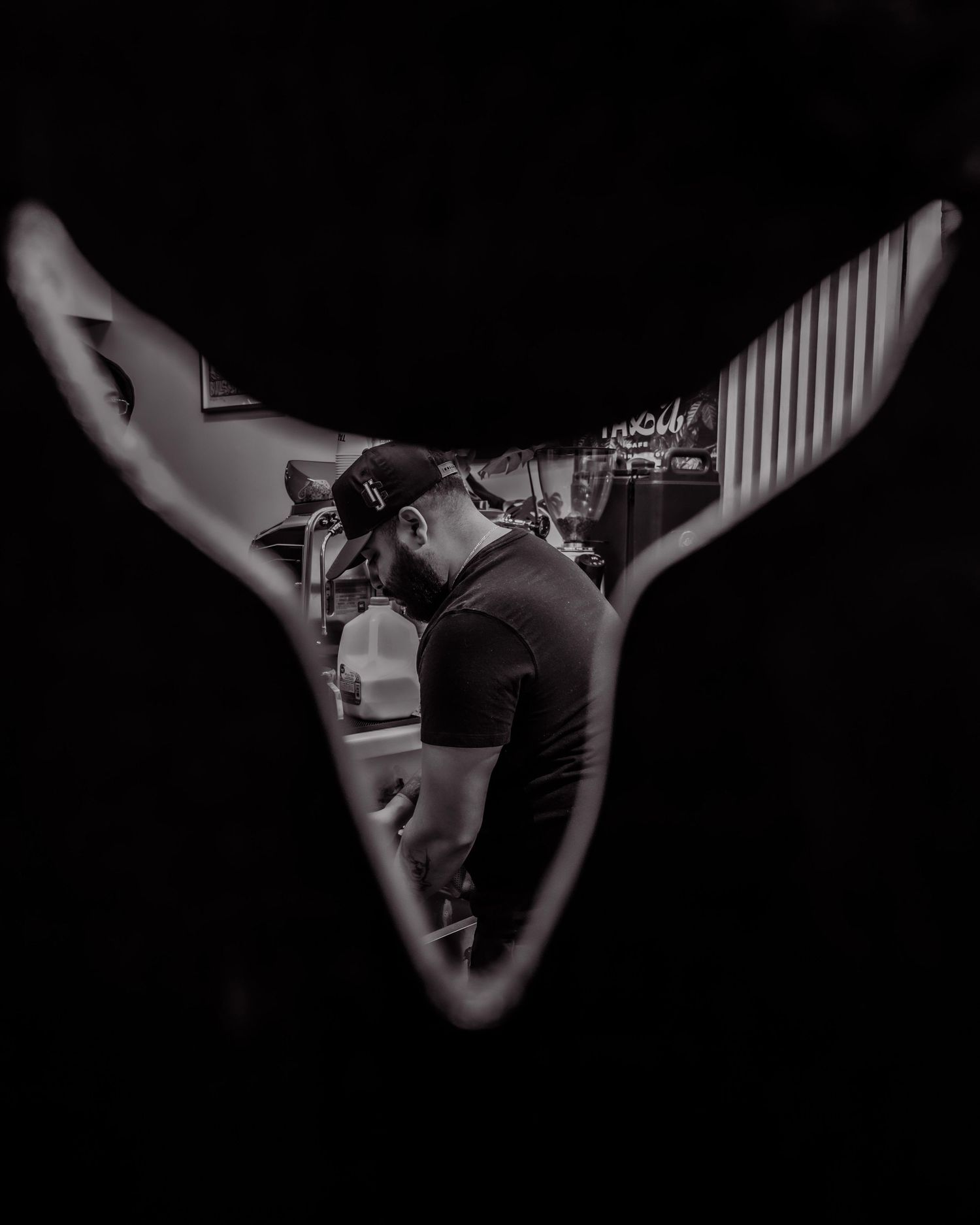 Black and white photo of a man in a cap viewed through a whale tail cutout shape.