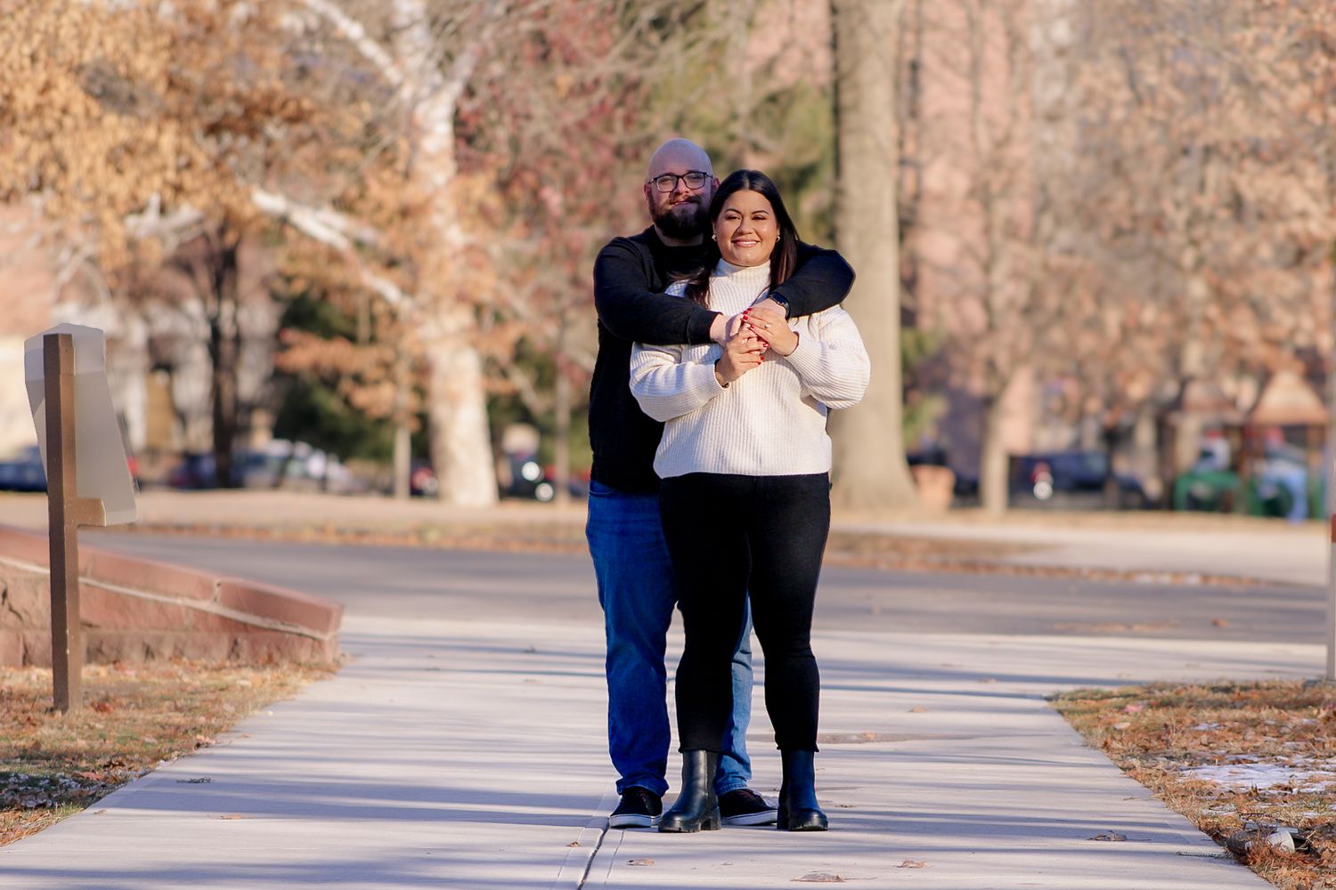 A couple in casual attire taking a romantic stroll along a tree-lined pathway.
