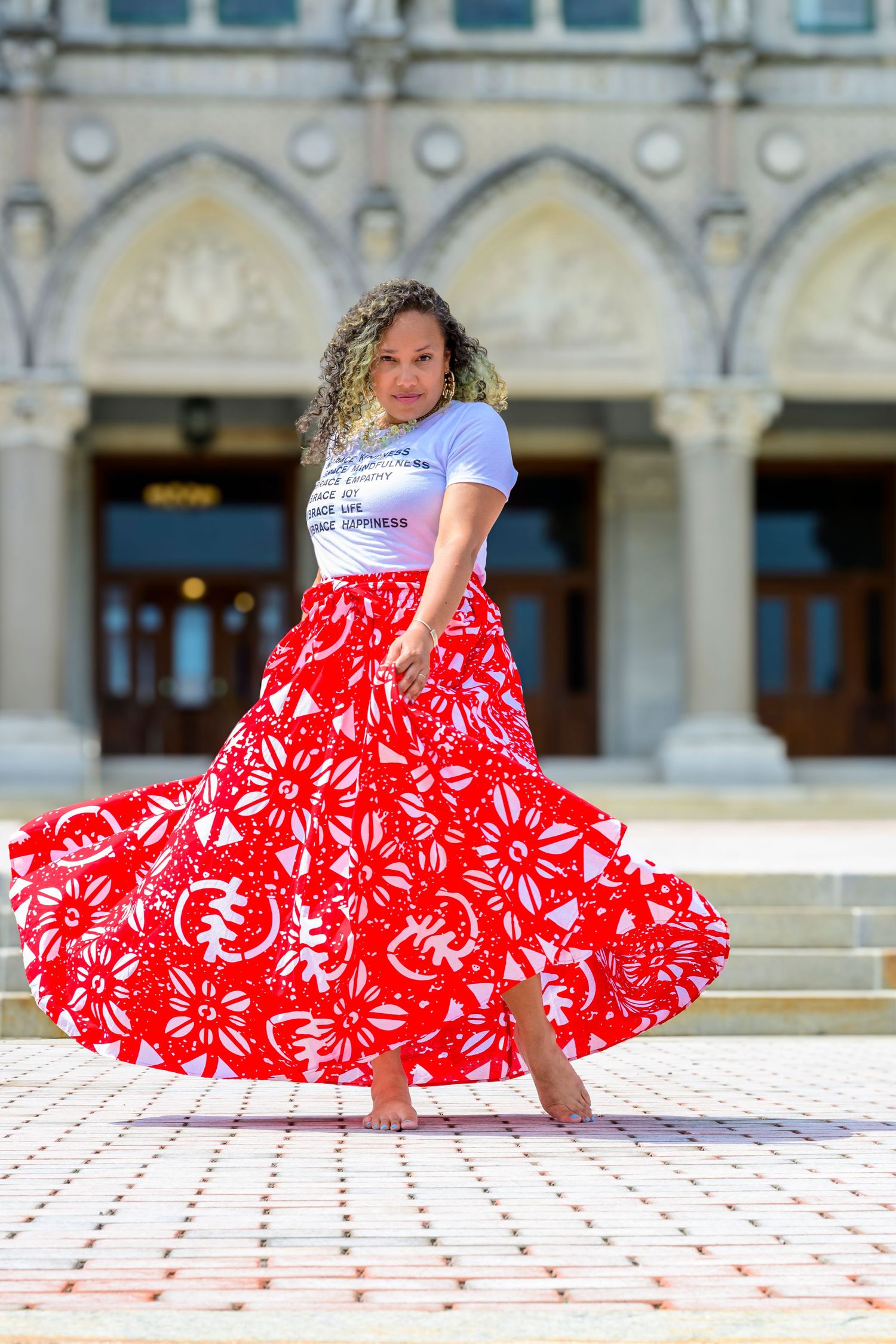 A flowy red and white floral maxi skirt twirls gracefully against an architectural backdrop with arched windows and pillars.