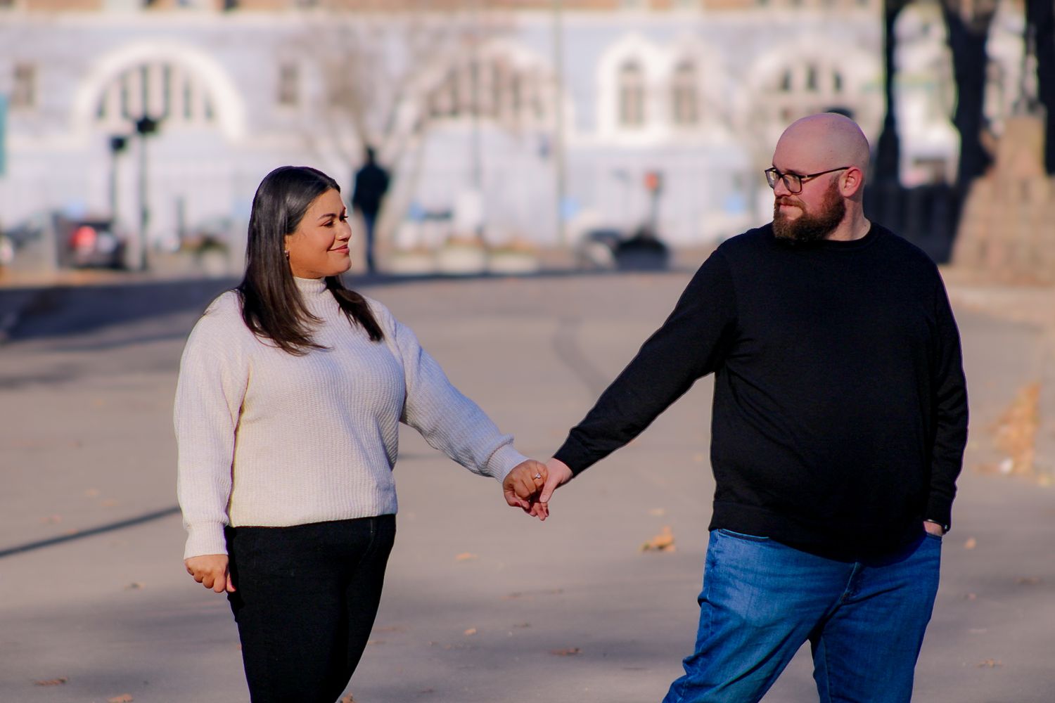 A couple walking hand in hand along a street with decorative architecture in the background.