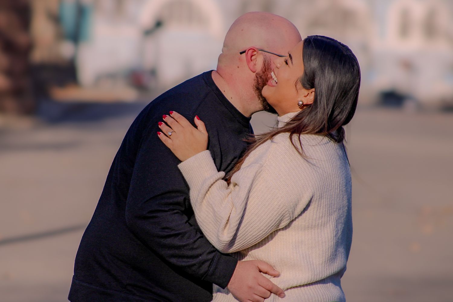 A couple shares a romantic kiss outdoors in warm light while wearing winter clothing.
