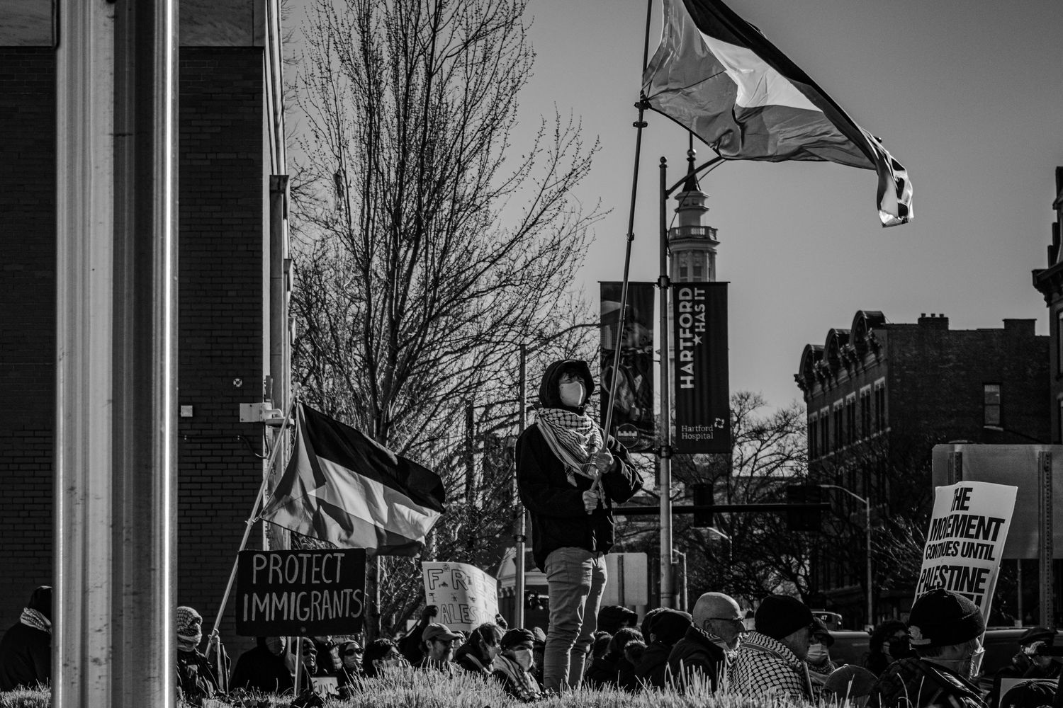 A black and white photograph of protesters waving flags and holding signs at a street demonstration.