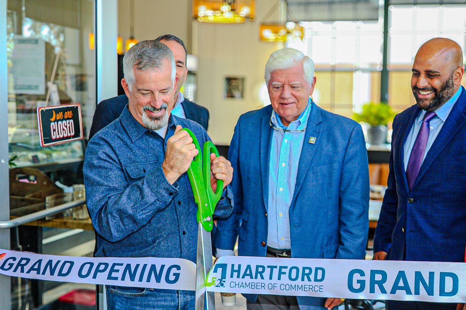 Three people participate in a ribbon cutting ceremony at a Hartford grand opening celebration.