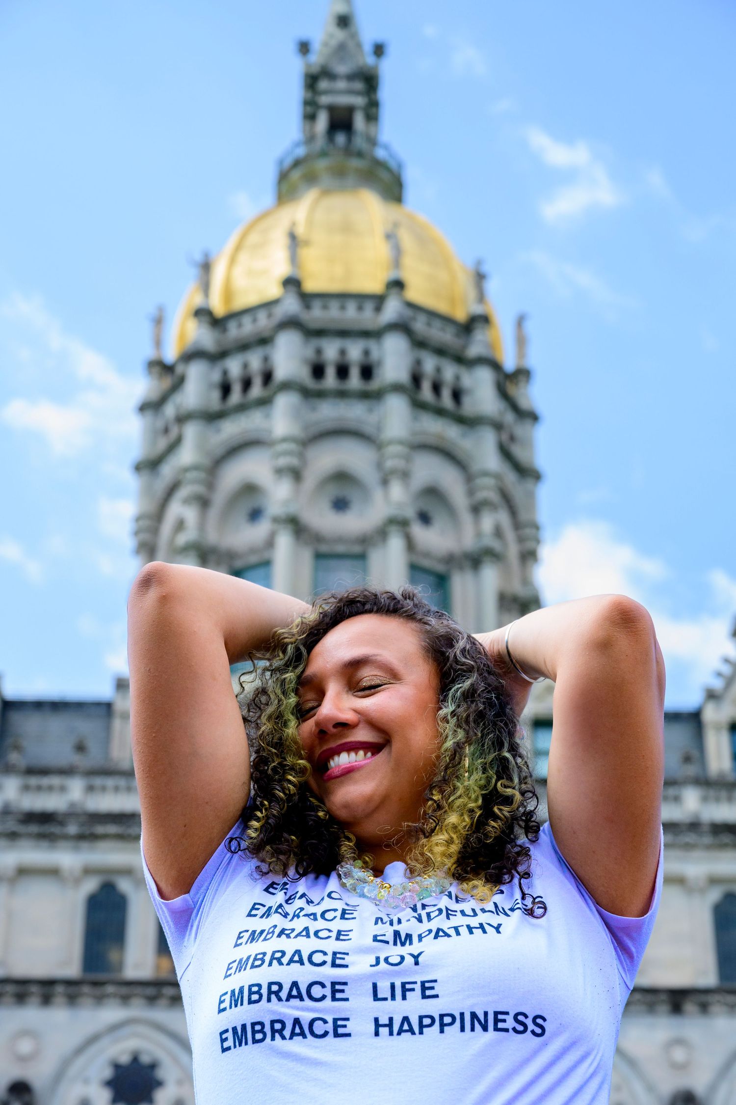 Person in white t-shirt with text 'Embrace Life' poses joyfully against ornate cathedral architecture in background.