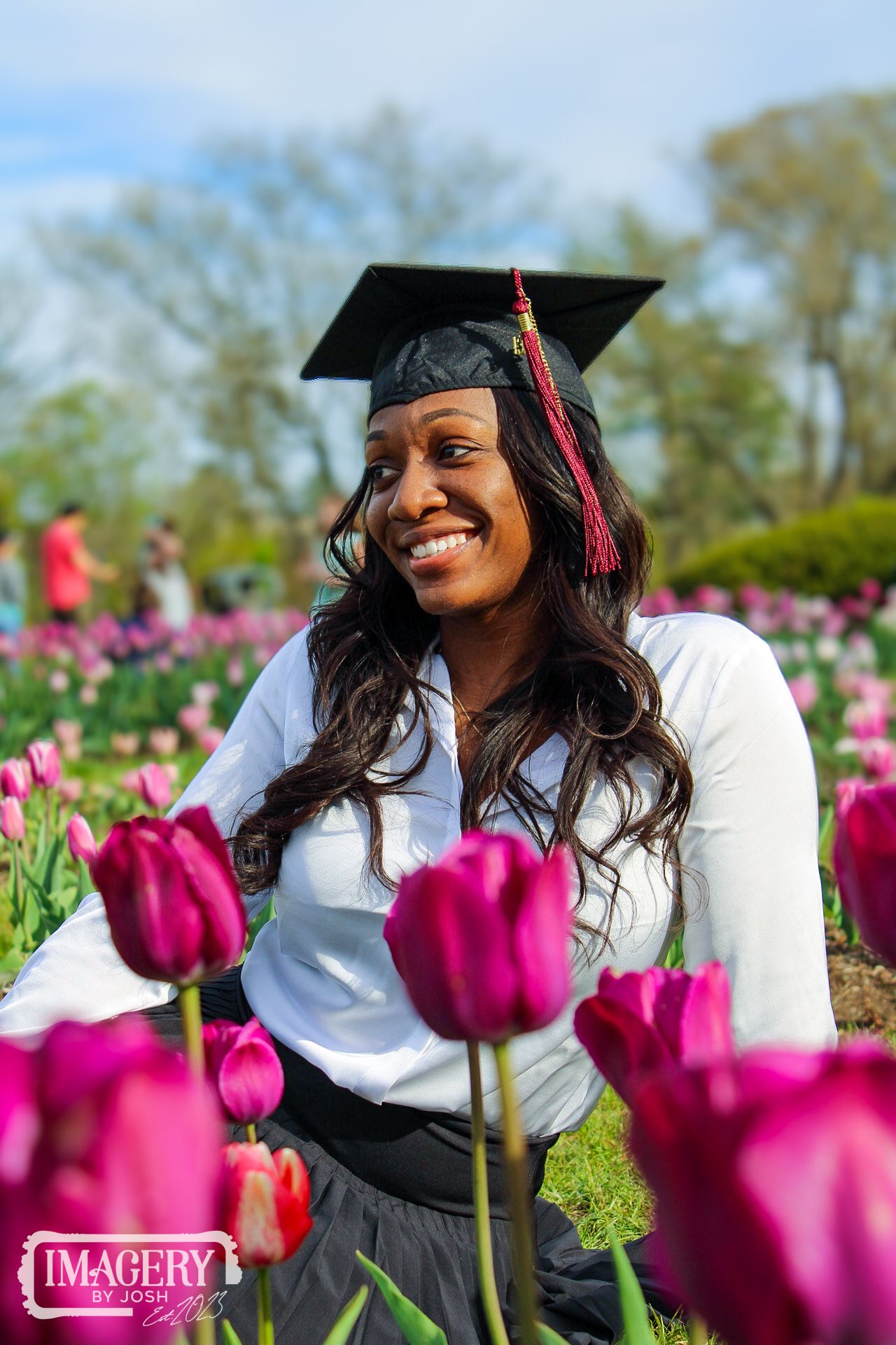 Graduate in cap and gown posing among vibrant pink tulips in a spring garden.