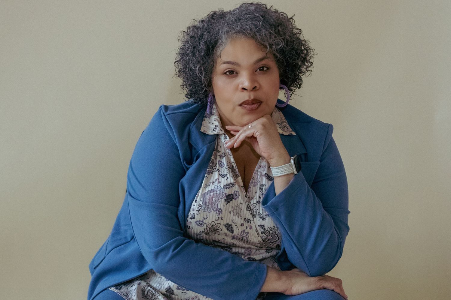 Professional in blue blazer and patterned blouse poses thoughtfully against neutral background.