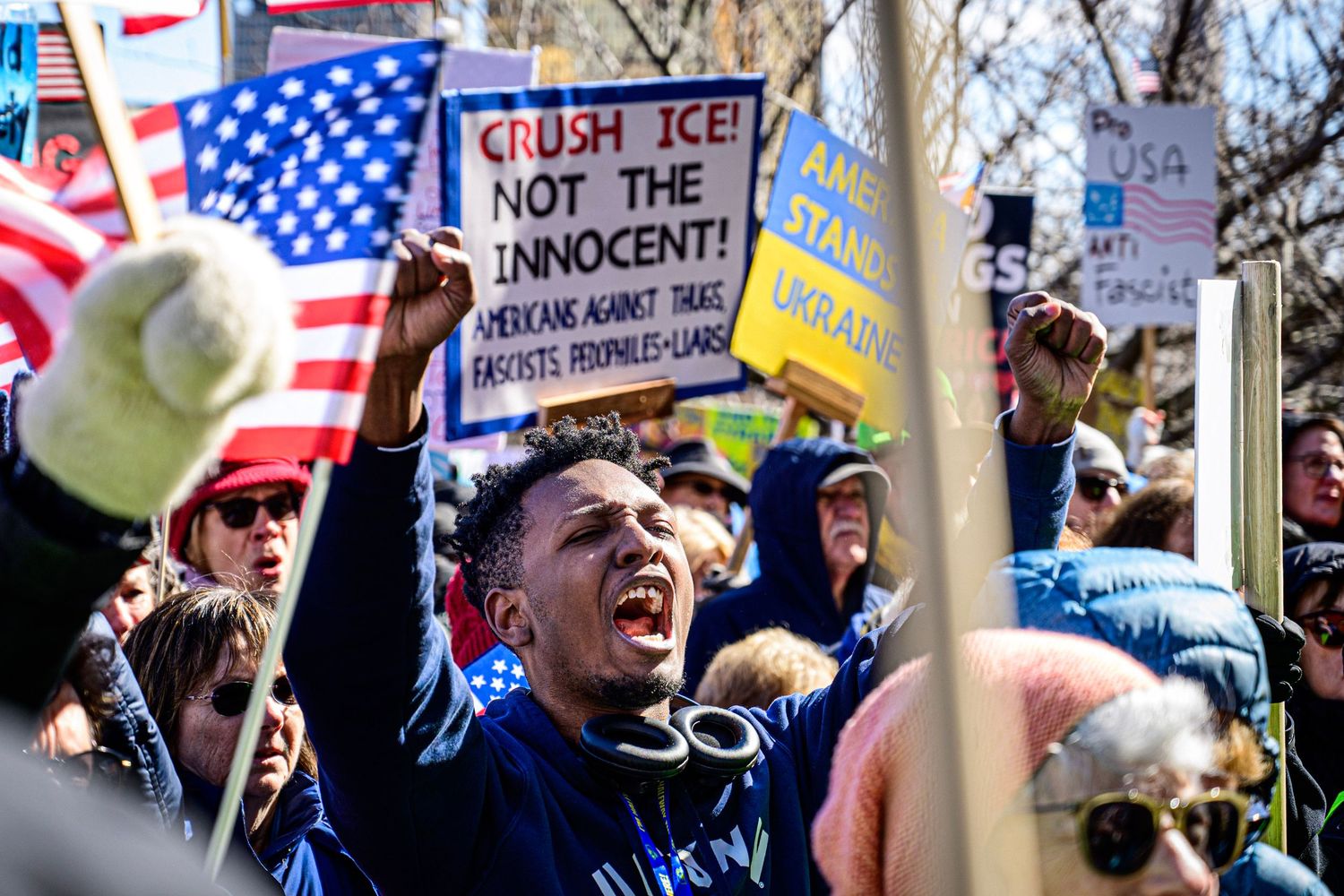 Protesters rally at outdoor demonstration holding signs including Crush ICE Not The Innocent at a crowded political protest.