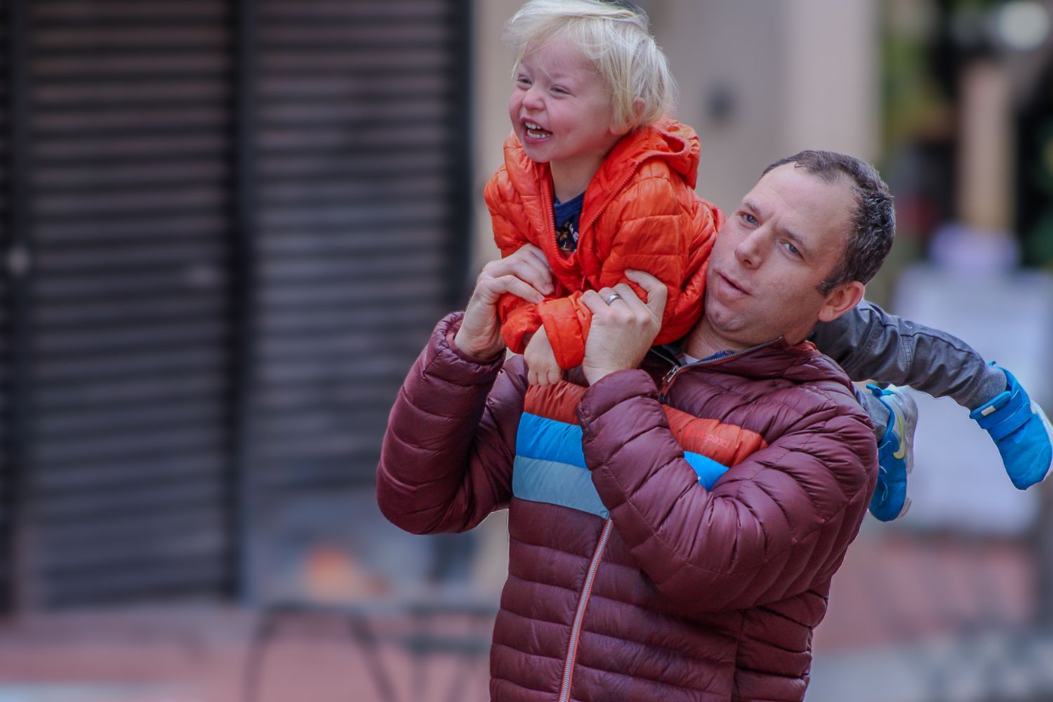 A playful moment of someone lifting a child wearing an orange jacket during outdoor playtime.