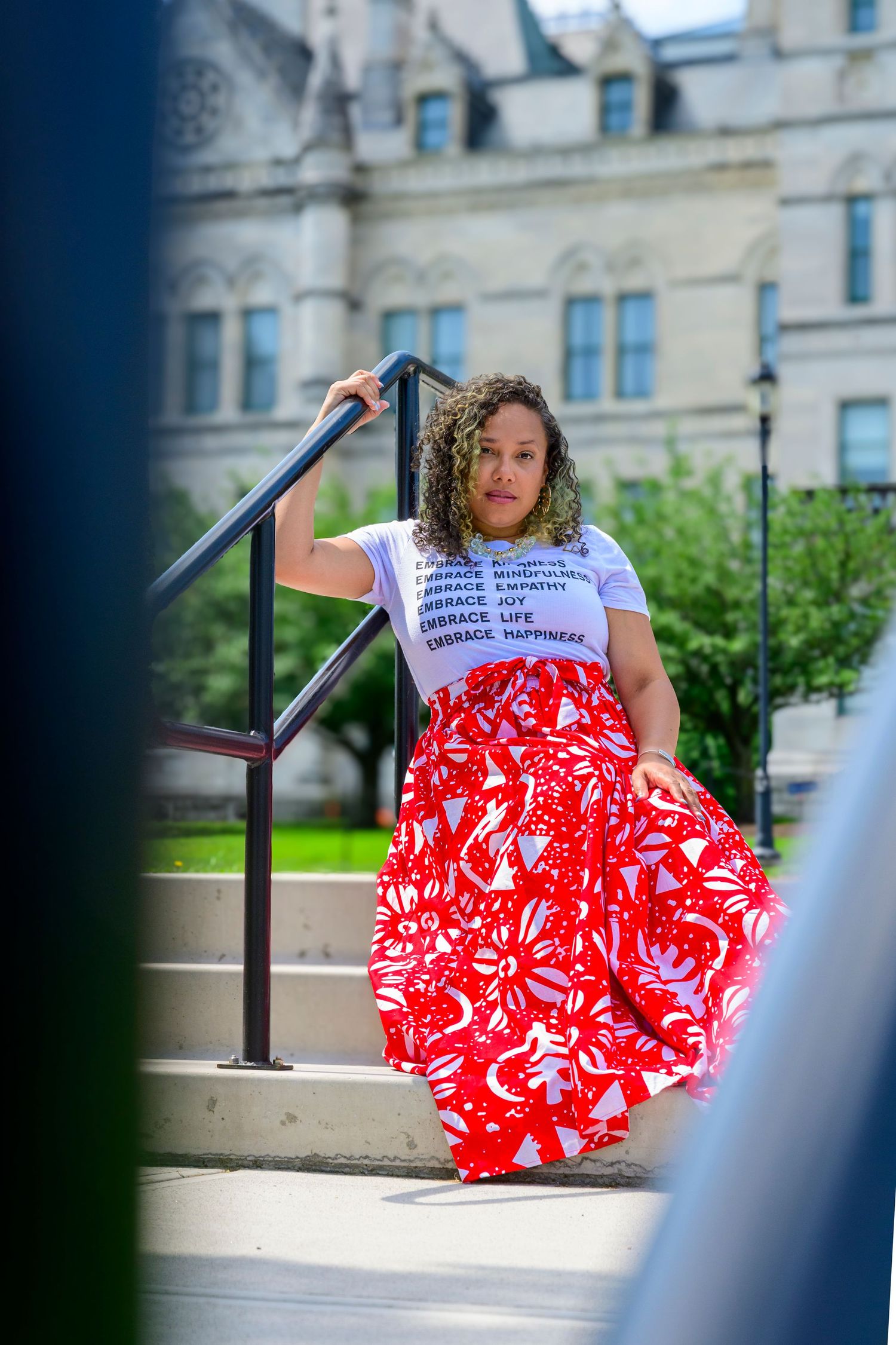 A person in a red and white floral dress sits on outdoor steps in a series of artistic poses.