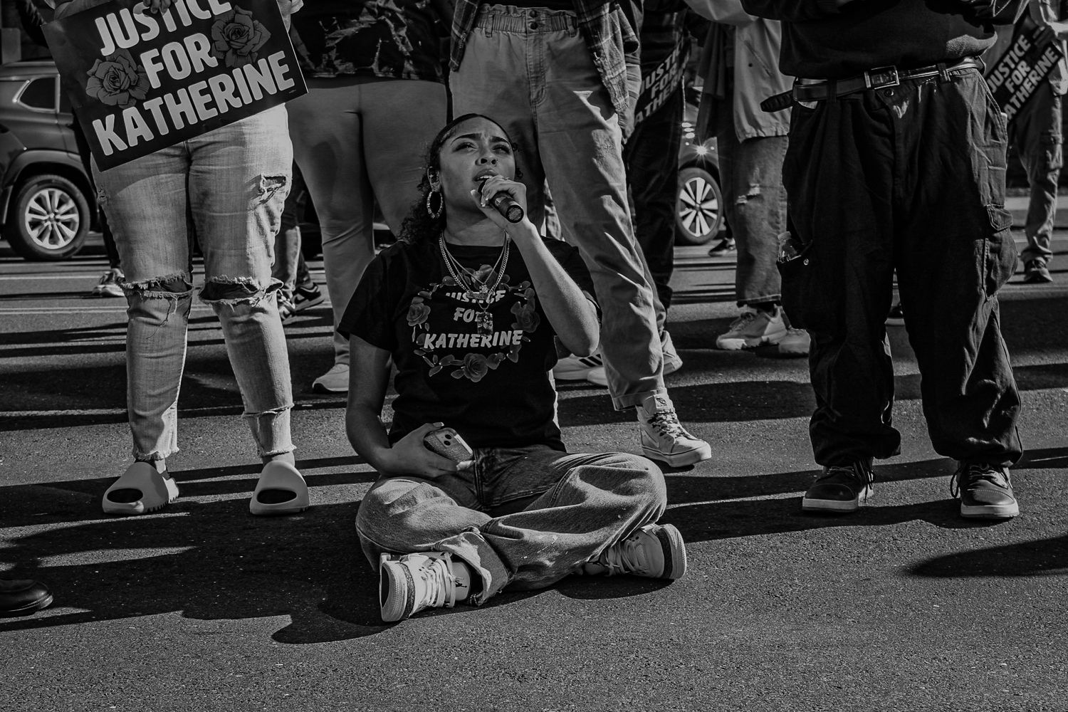 Protester sits cross-legged on street during demonstration holding justice sign.