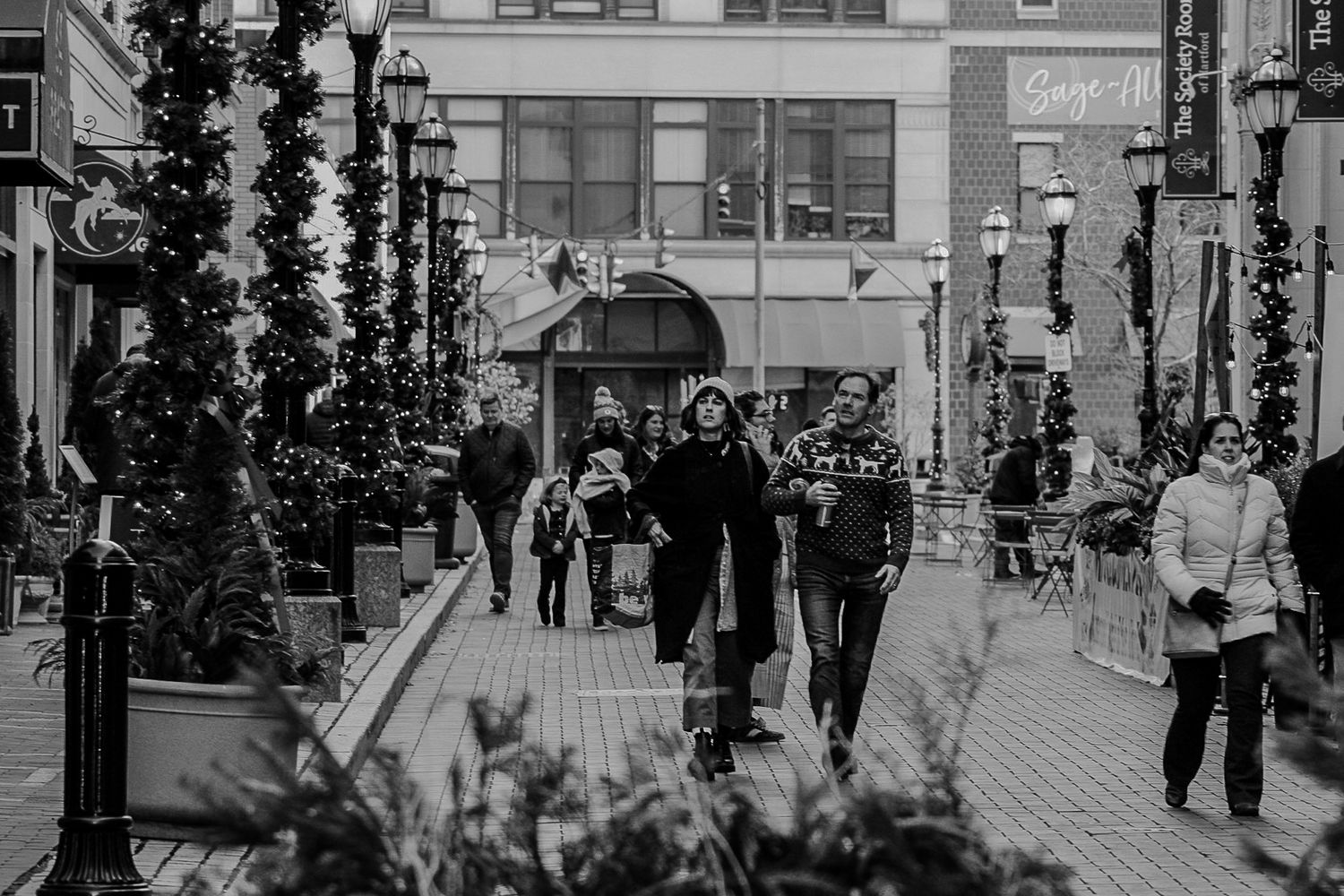 People walking down a decorated city street with trees and holiday decorations.