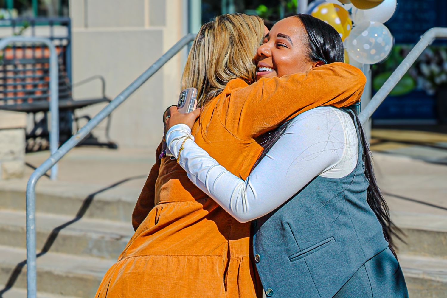 Two people share a warm embrace outside of a building with stairs.