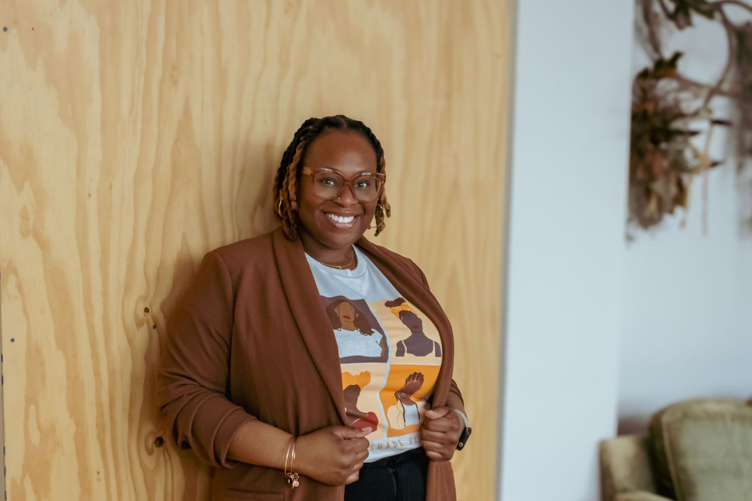 Person in brown cardigan smiling while holding cocktail glass against wooden wall.