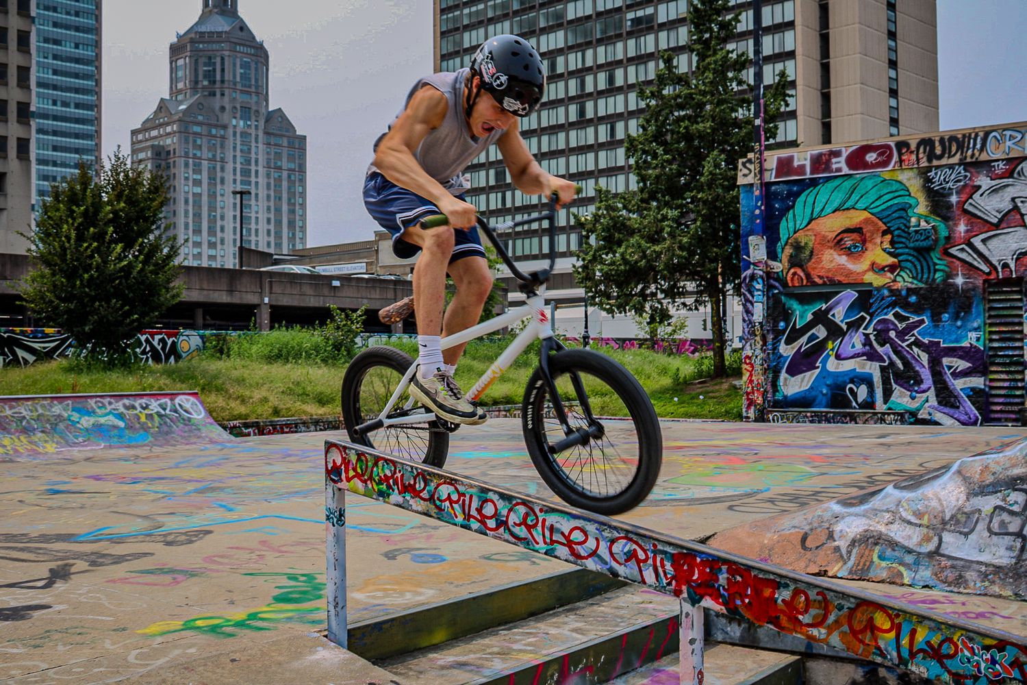 BMX rider performs trick on grind rail at urban skate park with colorful graffiti background.