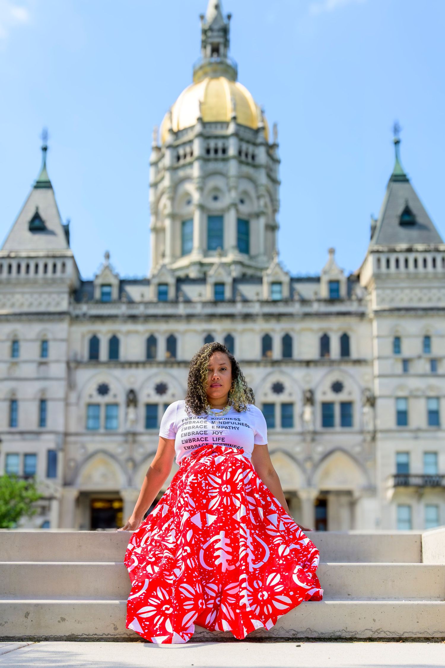Someone in a red and white patterned dress poses near a grand cathedral with ornate gold domes and Gothic architecture.