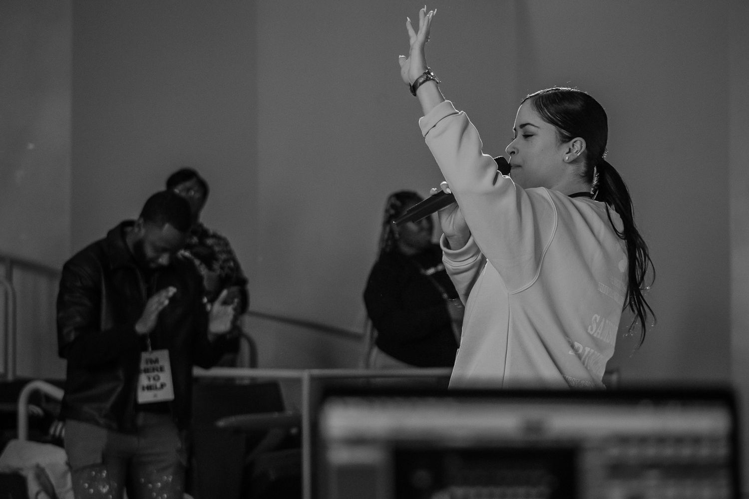 A performer in a white sweatshirt raises their arm dramatically during a dance routine captured in black and white.