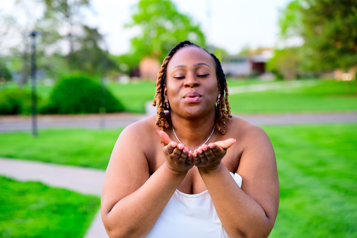 Woman in white blows a celebratory kiss while standing on a grassy lawn.