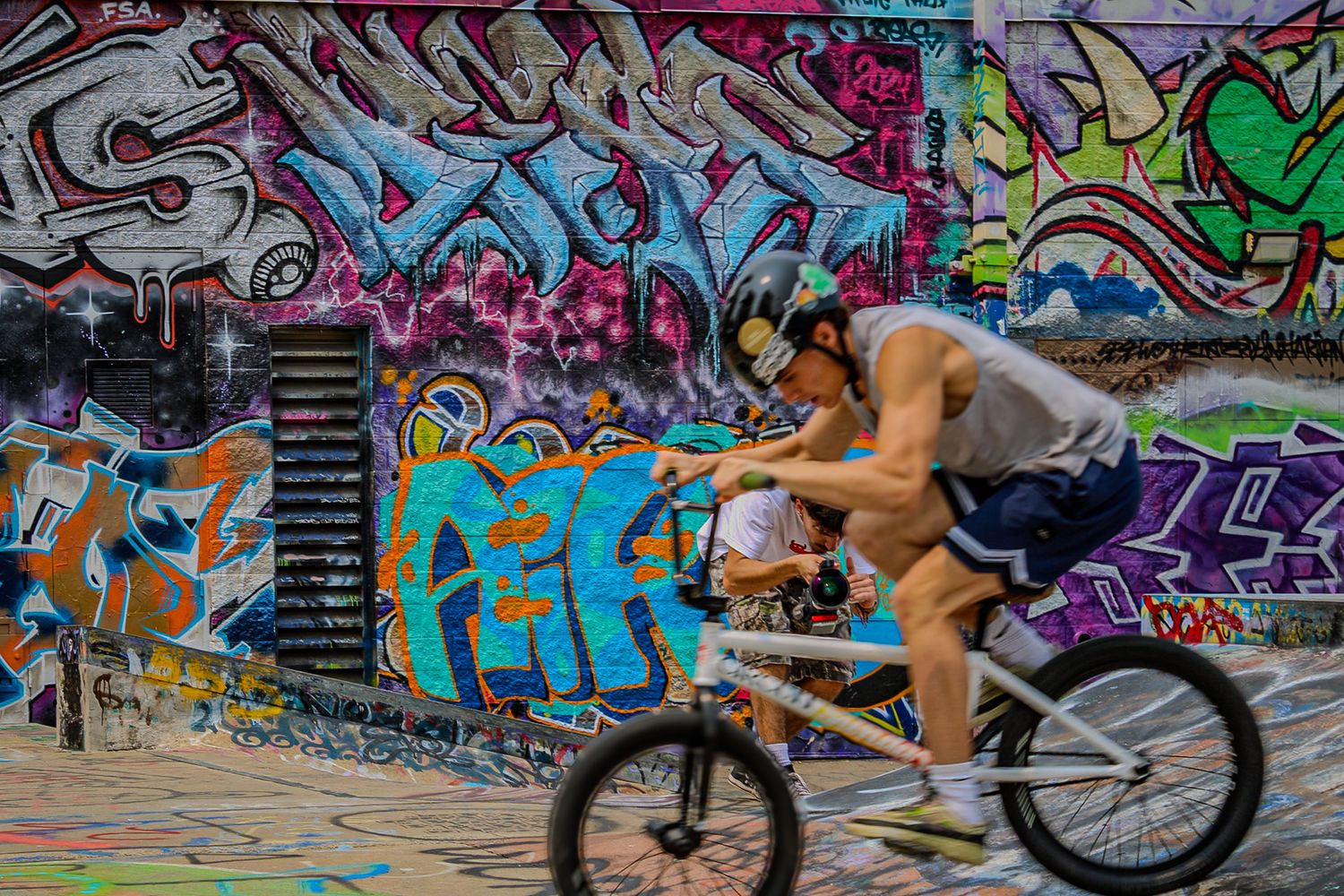 Cyclist rides past colorful graffiti wall in urban setting.