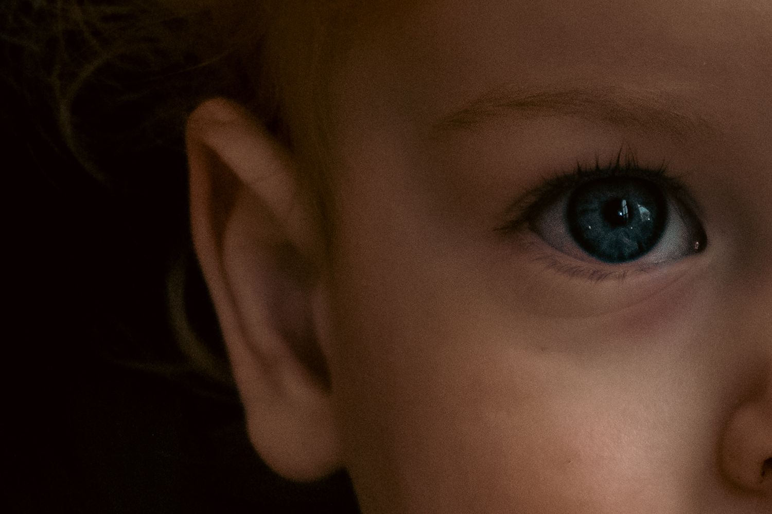 Extreme close-up of a bright blue eye and partial face in dramatic lighting.