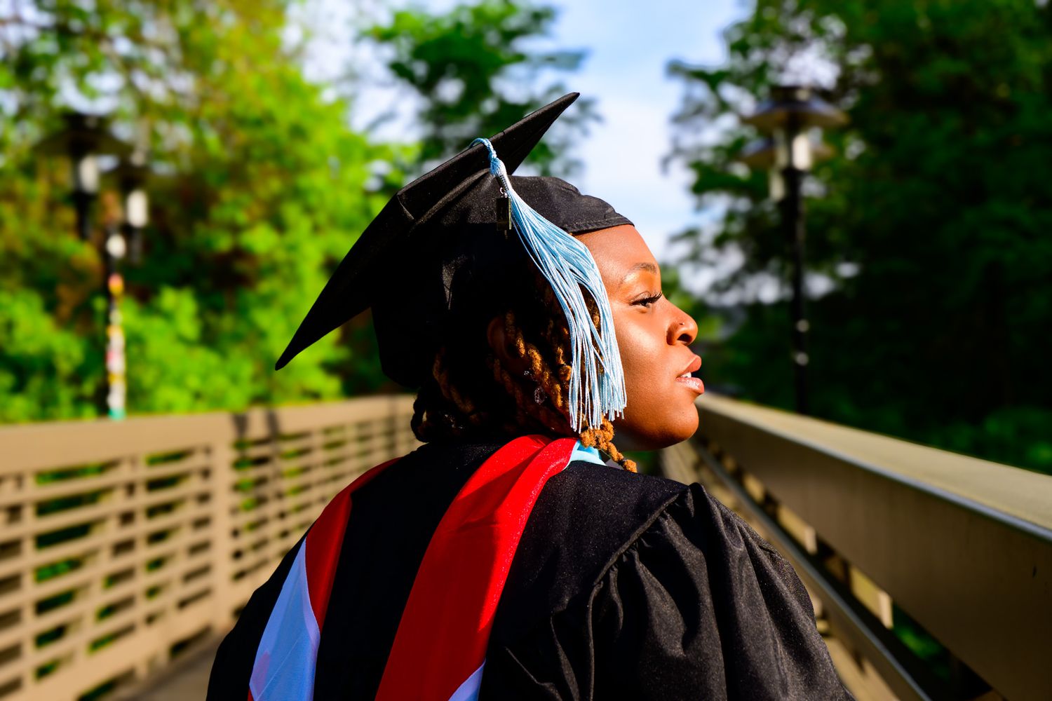 Graduate in cap and gown gazes thoughtfully into the distance on graduation day with a red sash.