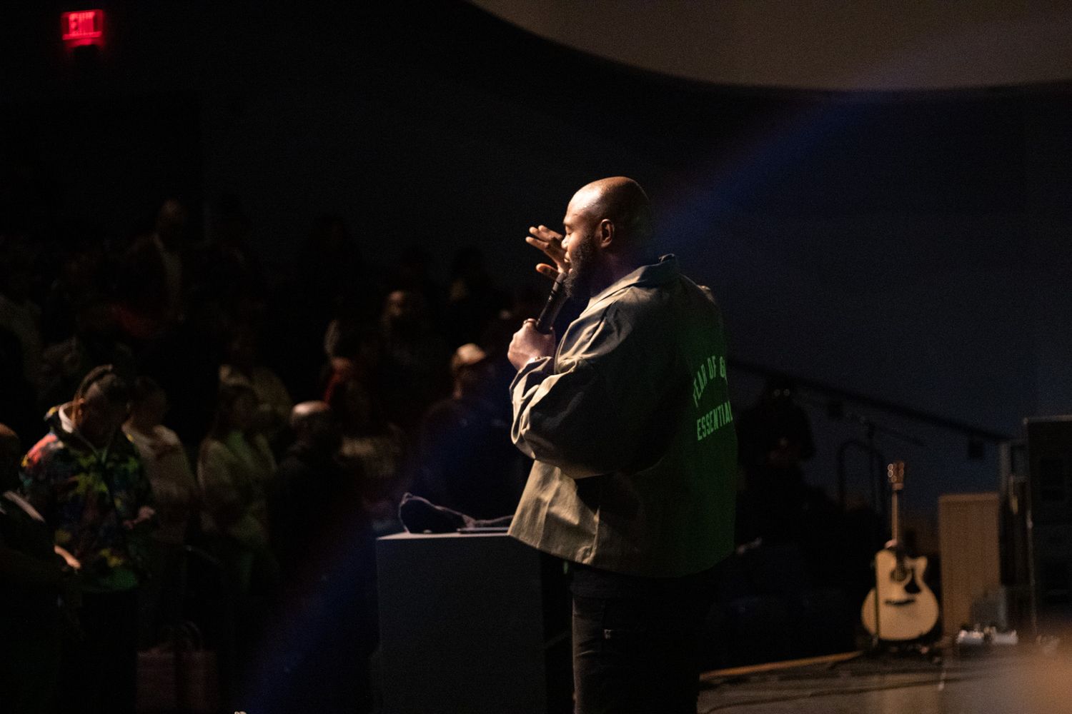 Speaker delivers presentation on stage with acoustic guitar visible in background.