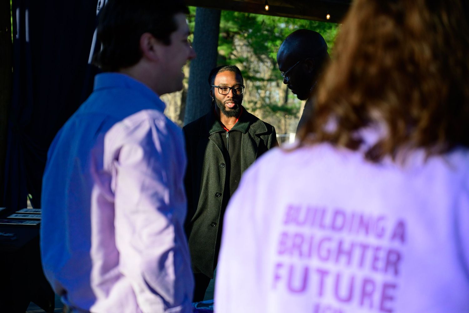 People at an event, one wearing a white shirt reading Building a Brighter Future, gathered in a dimly lit venue.