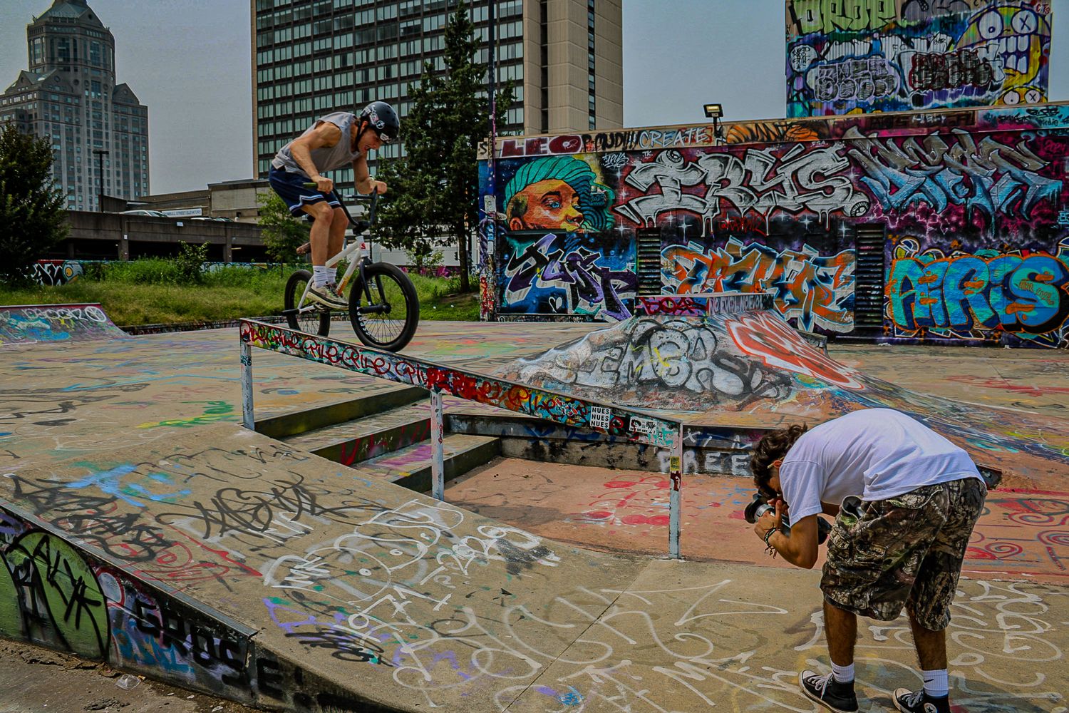 BMX riders perform tricks at skate park decorated with colorful graffiti.