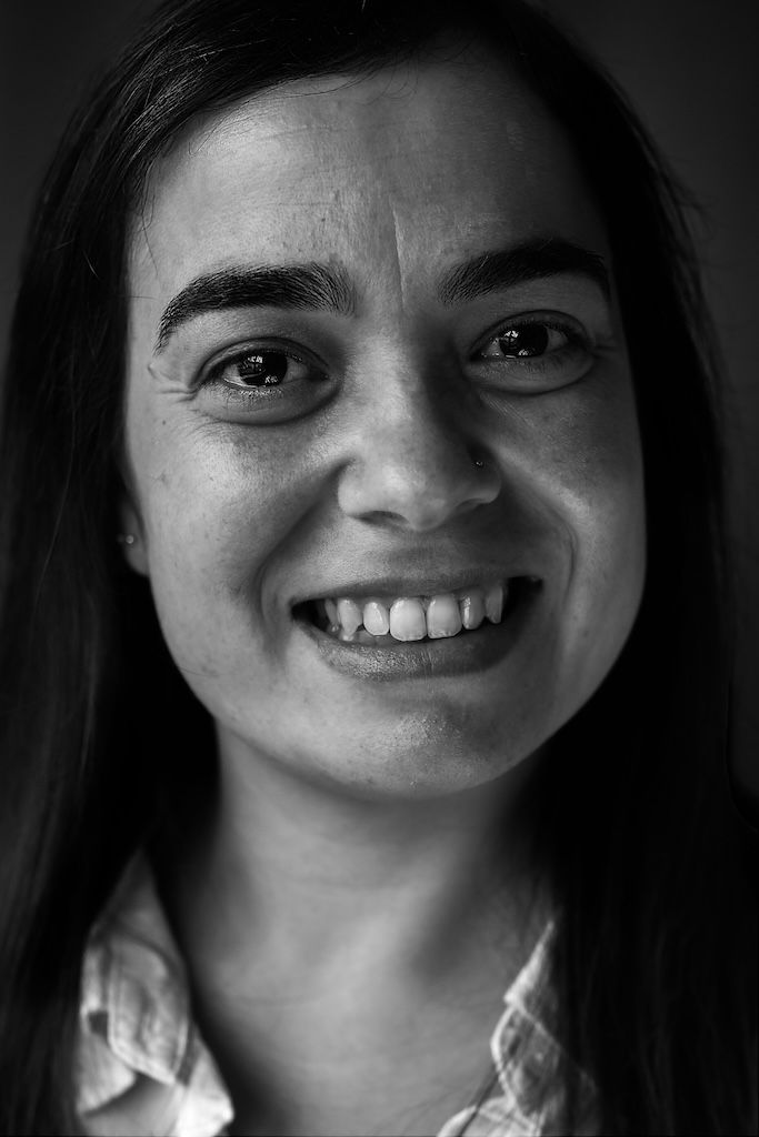 Zwart-witportret van een lachende jonge vrouw met lang donker haar, gekleed in een overhemd met kraag.
