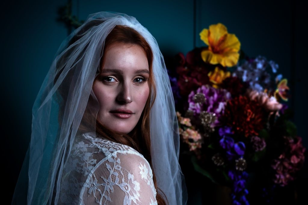 Een roodharige bruid, in een delicate kanten jurk en een doorschijnende sluier, bruidsboudoir fotografie zeewolde