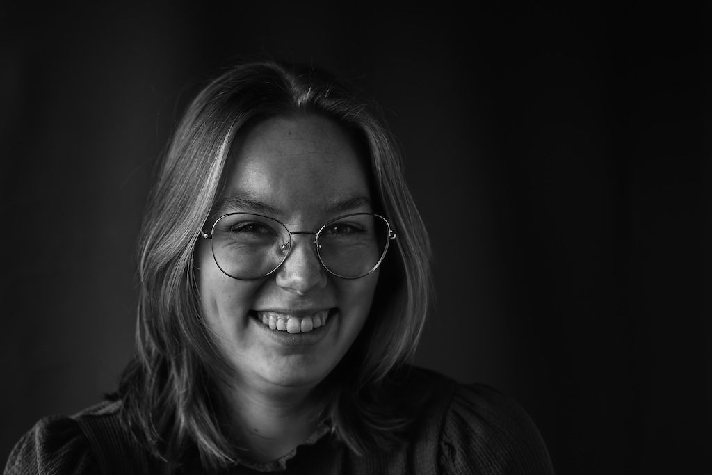 Lachende jonge vrouw met bril op een zwart-wit portretfoto.