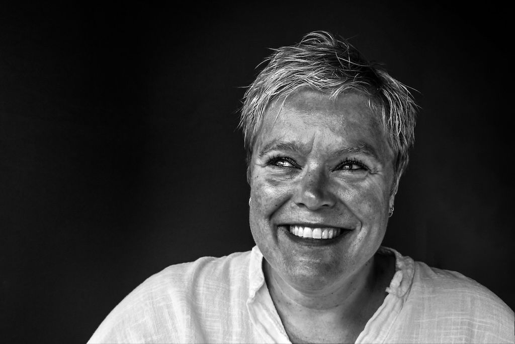 Zwart-witportret van een vrouw die hartelijk naar de camera lacht en een wit overhemd draagt.