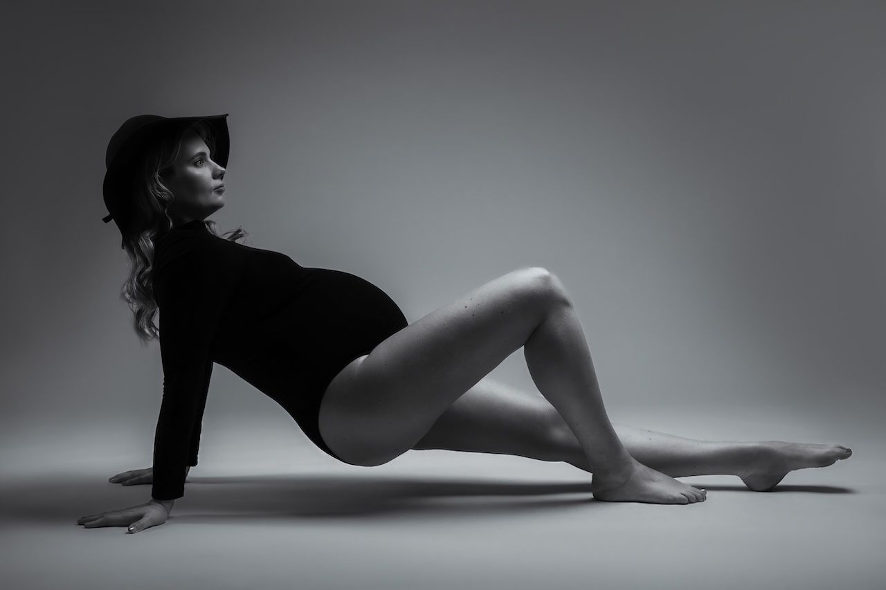 Zwangerschapshoot, zwangere vrouw die gracieus op de grond poseert in studio Zeewolde