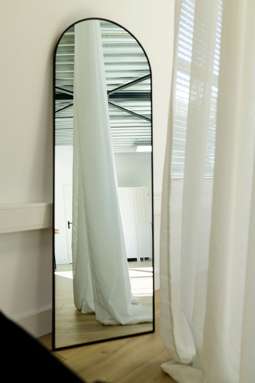 Minimalistisch interieur met witte gordijnen en een boogvormige spiegel die een serene, lichte sfeer creëren in fotostudio Zeewolde