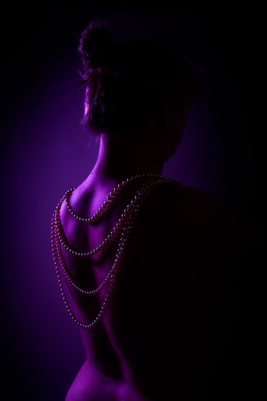 Silhouet rug met gedrapeerde parelkettingen tegen paarse verlichting in boudoirshoot Zeewolde