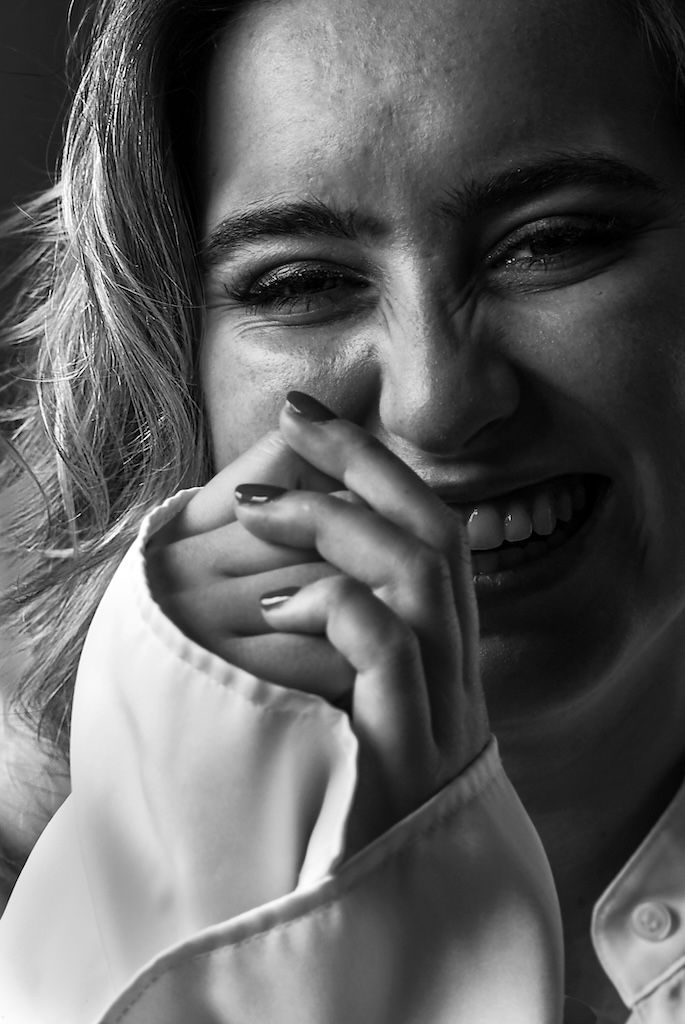 Zwart-witportret van een lachende vrouw die haar hand voor haar mond houdt en een witte blouse draagt.