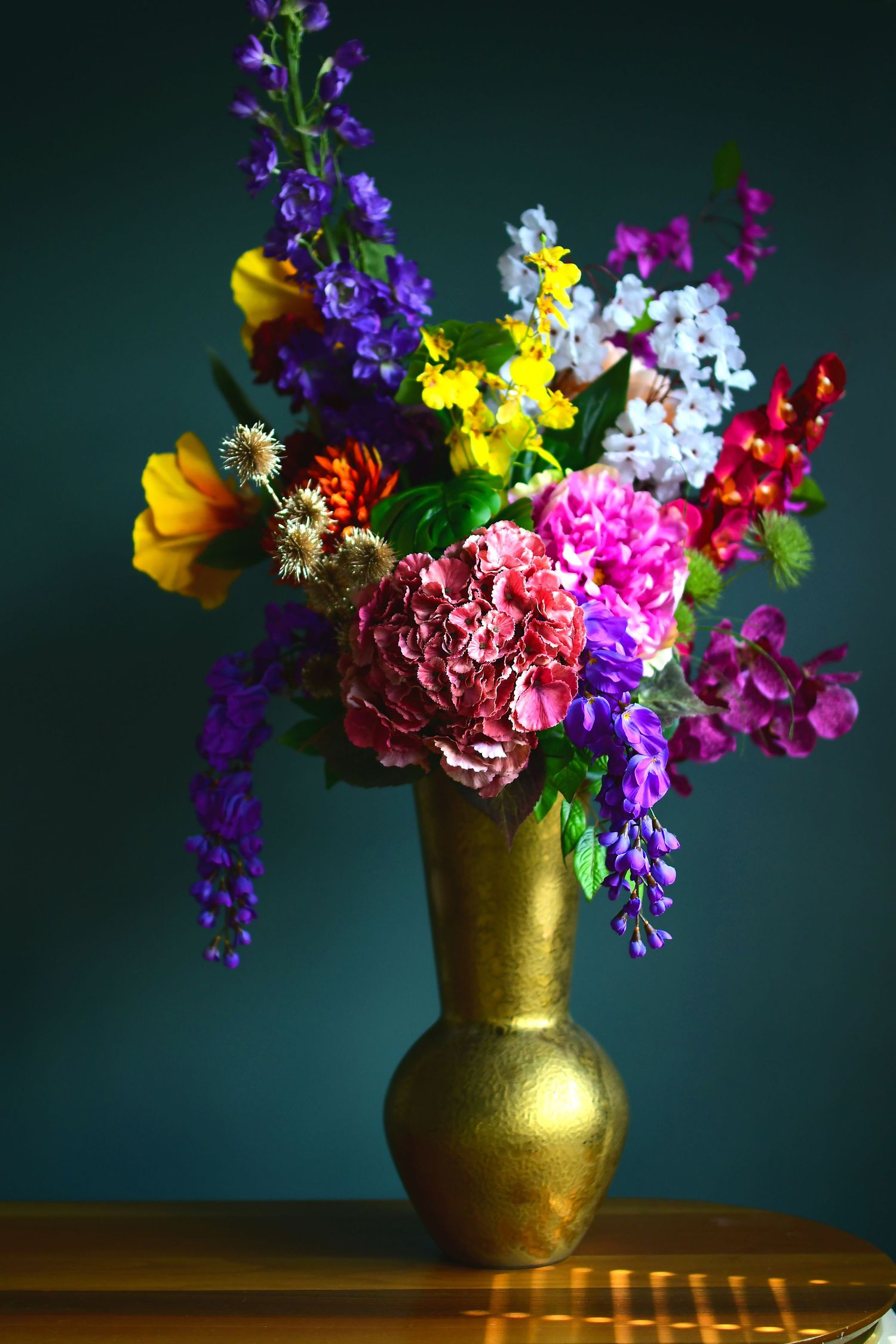 Levendige bloemen in een goudkleurige metallic vaas tegen een donkere achtergrond in daglichtstudio Zeewolde