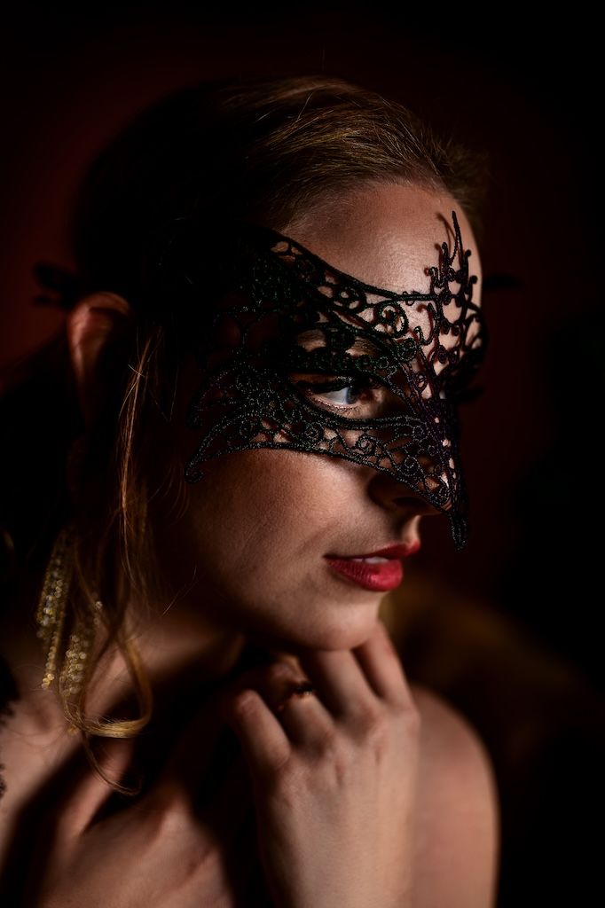 boudoirfotografie in zeewolde: Vrouw met een elegant zwart kanten masker en rode lippen.