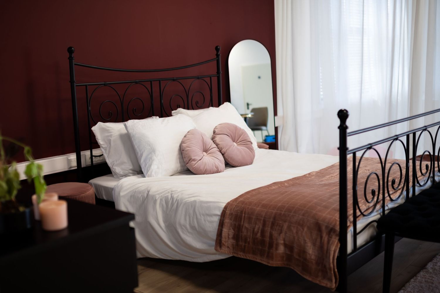 Knus slaapkamerinterieur met bedframe, wit beddengoed en zachtroze accenten tegen rode muur in daglichtstudio Zeewolde.