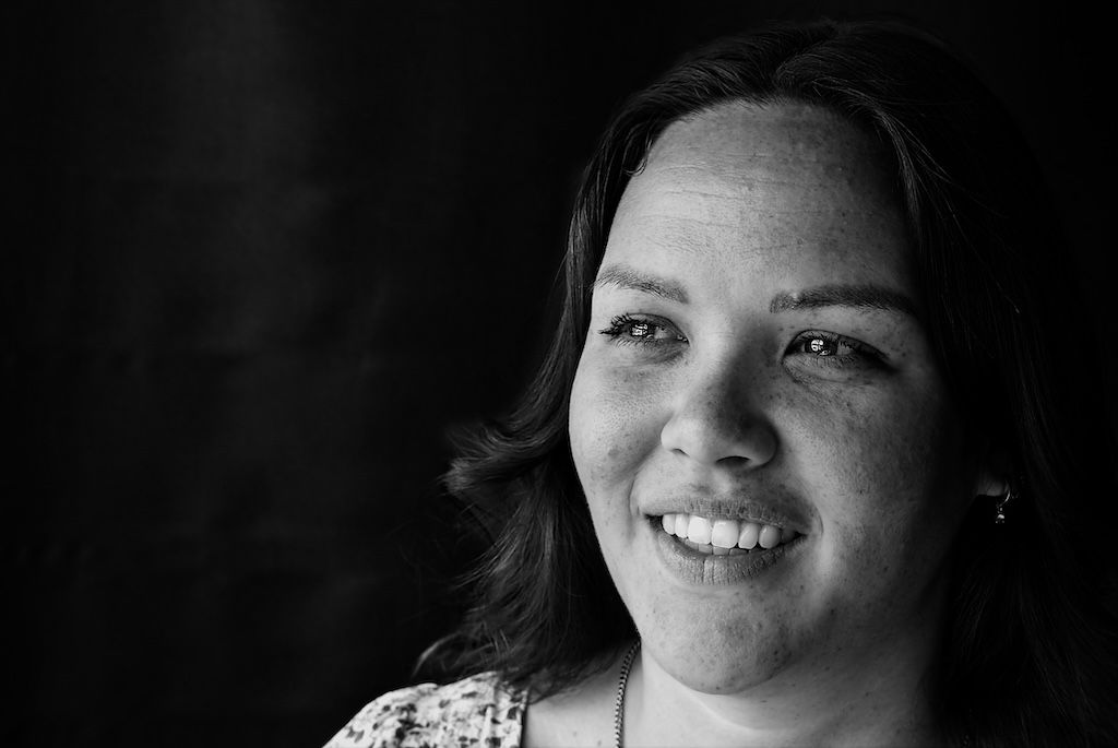 Zwart-witportret van een lachende jonge vrouw met sproetjes, gekleed in een bloemenblouse en kleine oorbellen.
