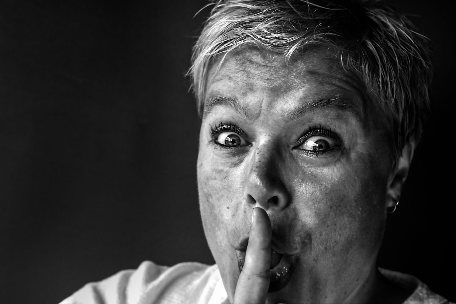 Zwart-witportret van een vrouw met de vinger tegen de lippen gedrukt als een gebaar van stilte.