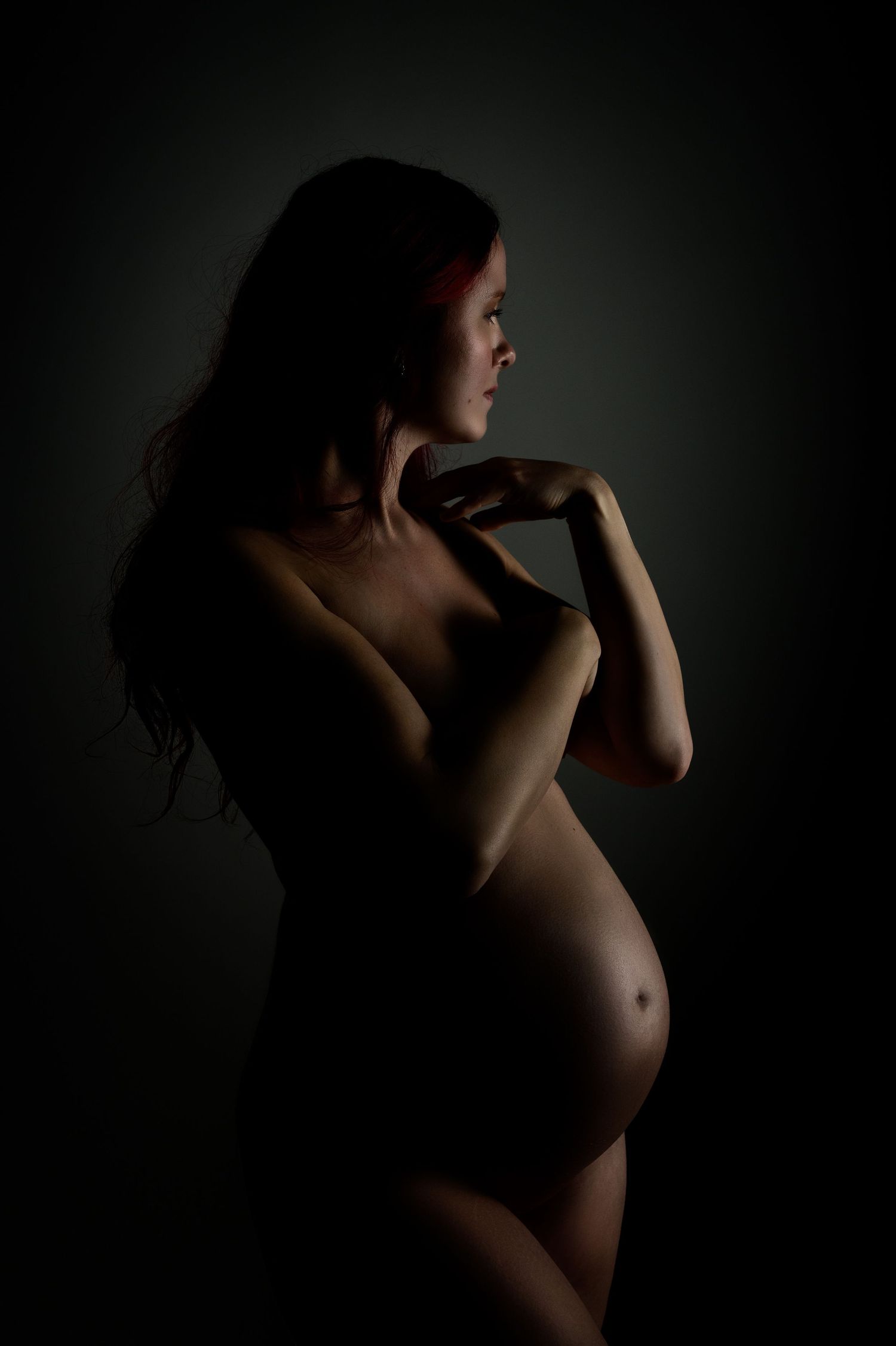 Artistic silhouette maternity photo showing an expectant mother's profile against a dark background.