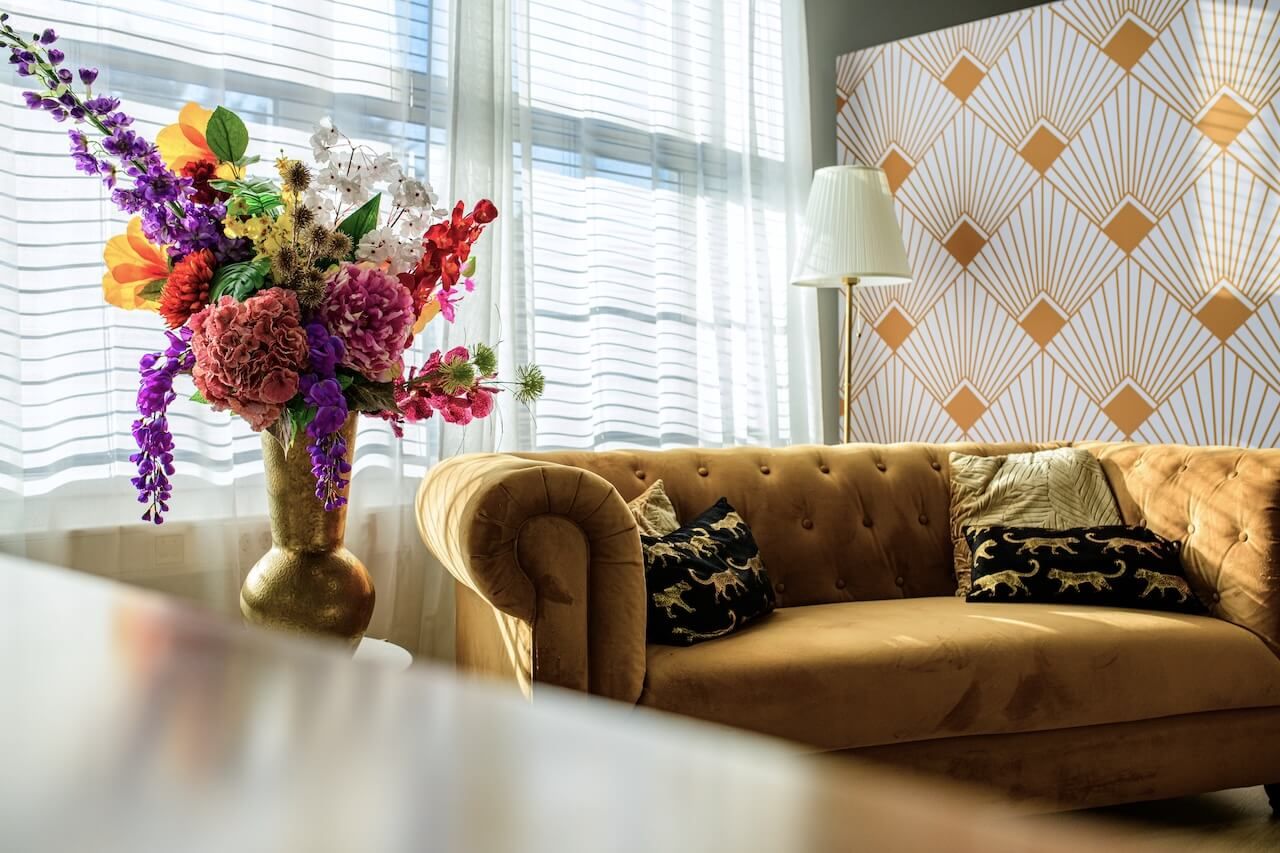 fotostudio Zeewolde met een kleurrijk bloemstuk op een tafel naast een fluwelen bank, met art-decobehang op de achtergrond.