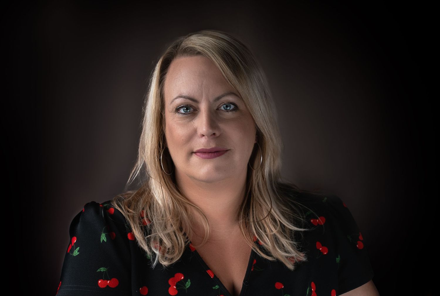 Studio portrait against dark background wearing black and red floral dress.
